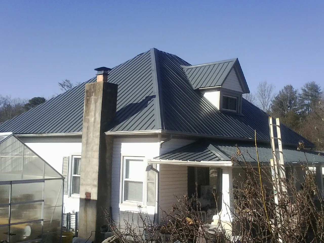 Dark blue standing seam metal roof on a white farmhouse with dormer — Slate & Tile Roof Repair by Roofing Brothers in Holden