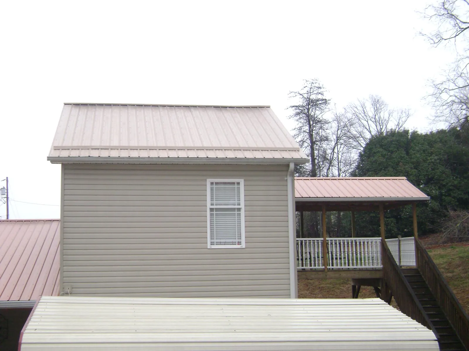 Tan metal roofs on a two story addition and attached porch, from a Roof Replacement job in Holden